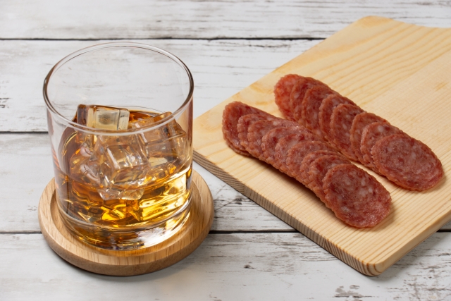 氷の入ったウイスキーロックグラスとカットされたサラミのおつまみ
