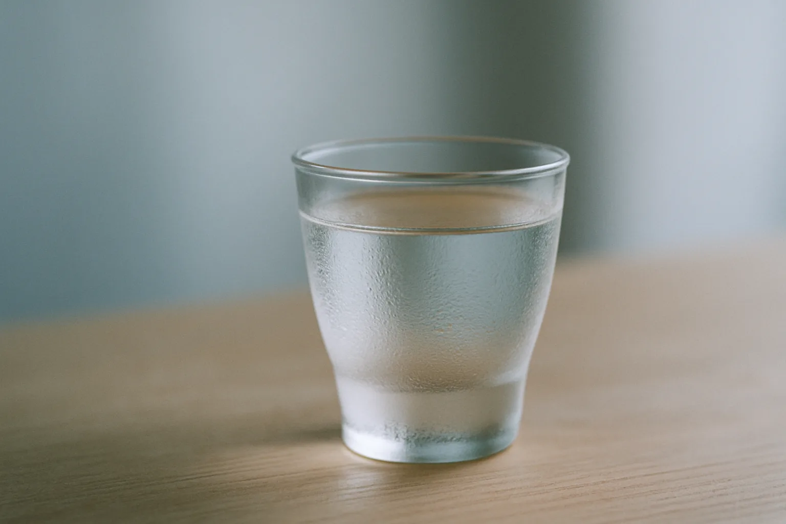 冷やした透明な日本酒が注がれた小ぶりのグラス。結露が付いた澄んだ液体のクローズアップ